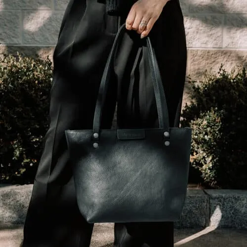 Woman wearing work attire holding a black leather shoulder bag with one hand.