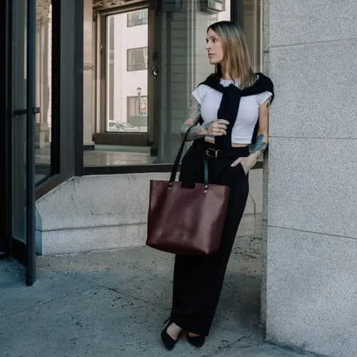 Woman wearing work attire holding a large sangria-purple leather shoulder bag on her arm.