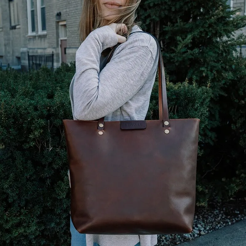 Woman carrying a large, brown leather shoulder bag on her shoulder.