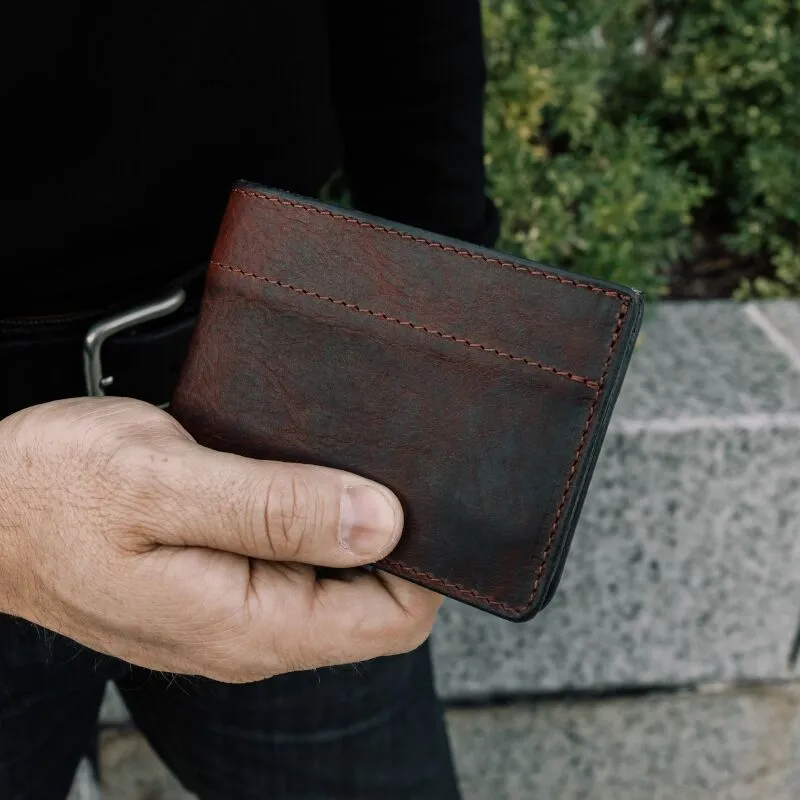 Close up photo of a man holding a dark reddish brown leather wallet to show the detail of the outside cover.