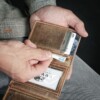 man pulling out card from trifold wallet in vintage brown leather