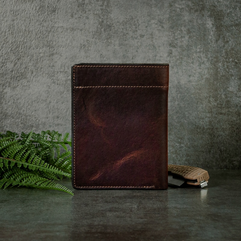 Man made dark red passport wallet that holds your passport, cash flow and cards shot on a grey slate background with ferns and pocket knife.
