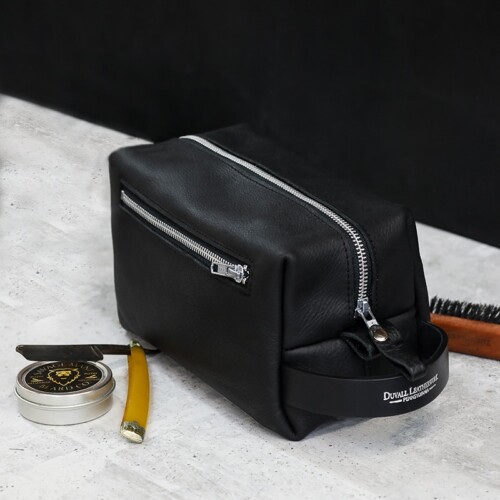 A handcrafted, black leather toiletry bag zippered closed