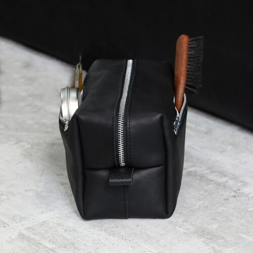 A black leather dopp kit bag, unzpped to reveal nylon fabric lining inside