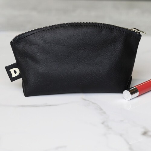 A small black leather makeup bag with a letter "D" brand tag