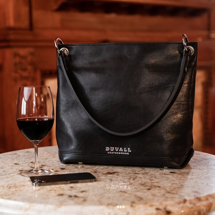 A women's black leather slouch bag displayed on a marble cafe table with red wine