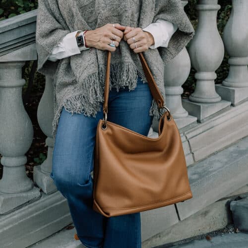 A closer look at a woman holding a tan leather slouch bag.