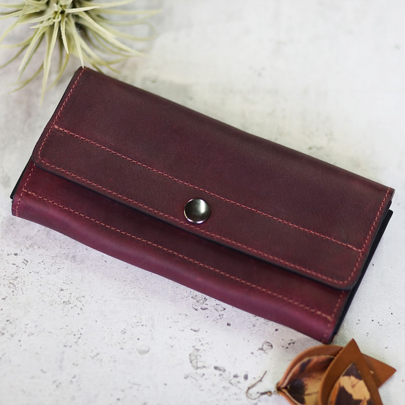A deep red wine-colored women's leather wallet shown closed wiht a brushed silver button snap