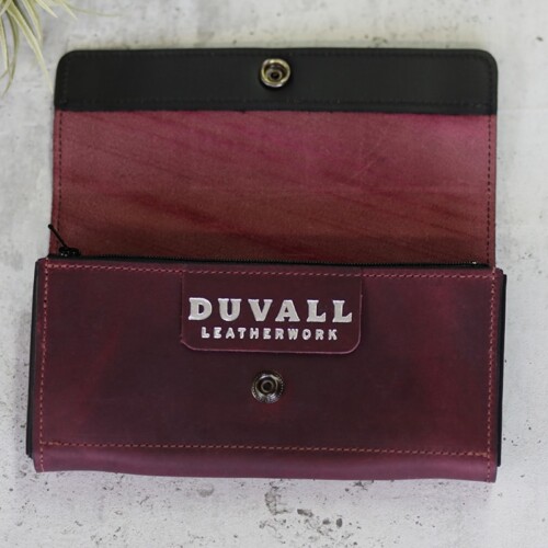 A rich women's purple leather wallet shown open to highlight black trim accent along the top edge
