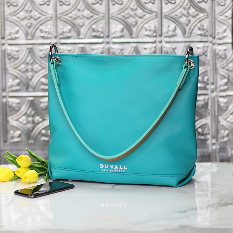 A turquoise leather women's purse, displayed on a marble counter against a punched tin backdrop