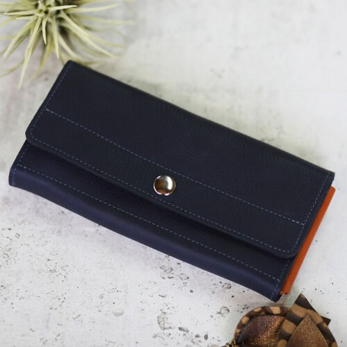 Women's deep blue leather wallet with orange folds shown closed with the silver button snap fastened