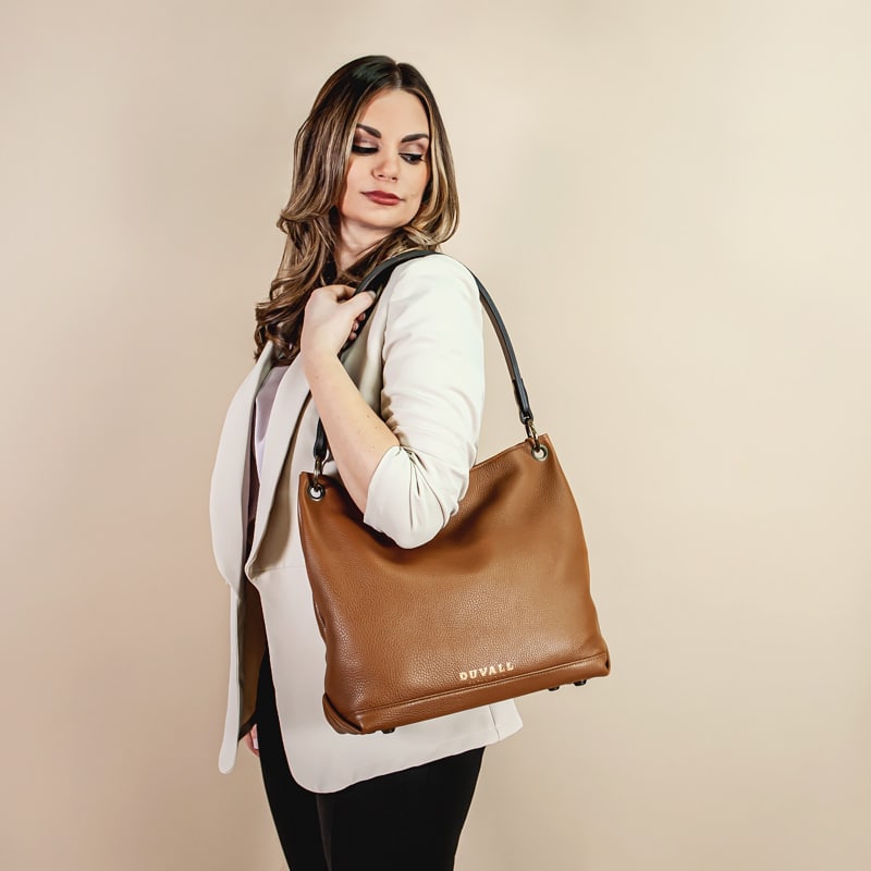Woman holding a slouch bag over her shoulder in front of a tan backdrop.