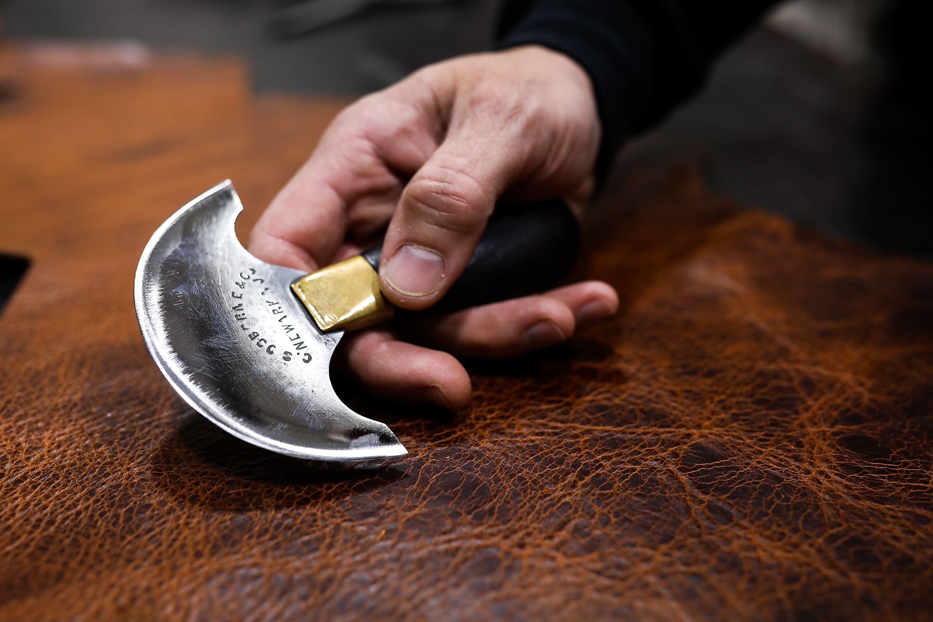 Person holding a round head knife with a bison cowhide on a table