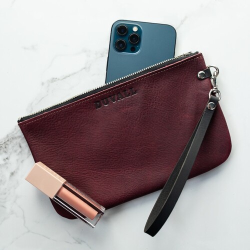 A sangria purple leather wristlet with a blue iPhone and a pink lip gloss.