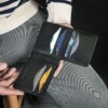 Man in stripe sweater showcasing black ID window bifold walletholding many credit cards