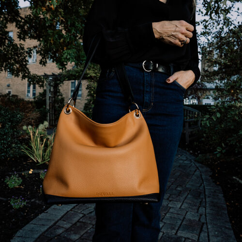 A close up of a honey and black leather slouch bag being held by a woman wearing a black blouse and dark jeans.