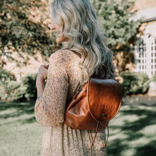 model wearing brown leather backpack purse outdoors surrounded by trees