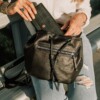 model holding black leather backpack purse and inserting a large women's wallet into the main compartment