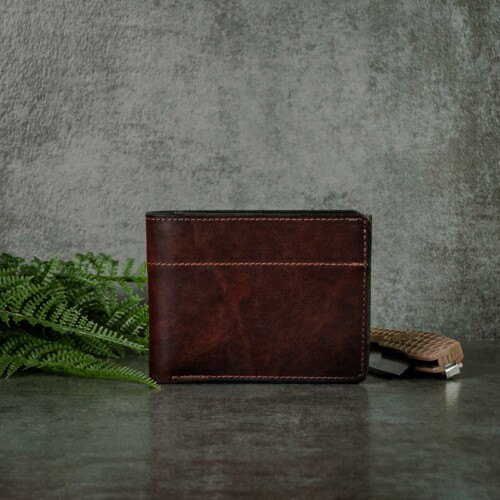 Very masculine dark mahogany bifold wallet that's made to last photographed with greenery and a pocket knife.