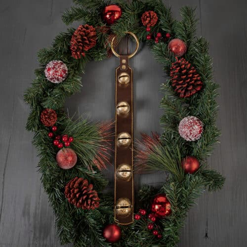 A brown leather door hanger with five brass bells laying on a Christmas wreath.