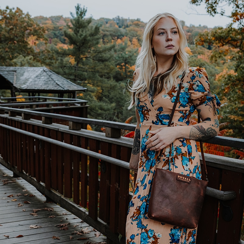 Woman modeling a brown leather crossbody purse on beautiful fall day