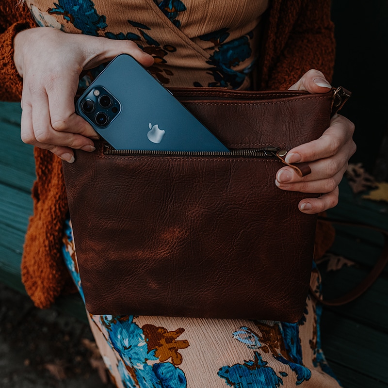 Woman pulling her phone out of pocket on a red brown crossbody bag