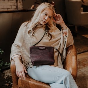 woman sitting with a sangria purple crossbody bag from duvall leather