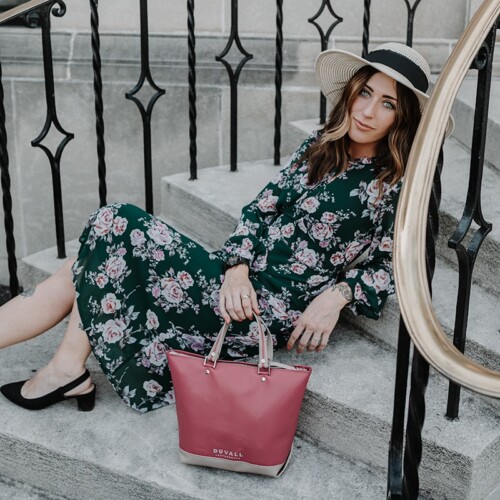 Woman in green dress and pink flowers posing on steps holding a perfect size pink purse made in America.