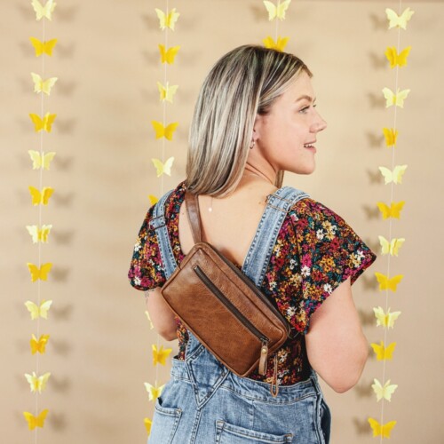 model wearing belt bag across her back and looking over her right shoulder with a tan background and yellow butterfly decorations