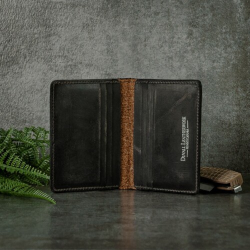 Inside of a credit card wallet that shows multiple slots for your cards and put cash in inner pockets shot with greenery leaves, pocket knife on a slate background.