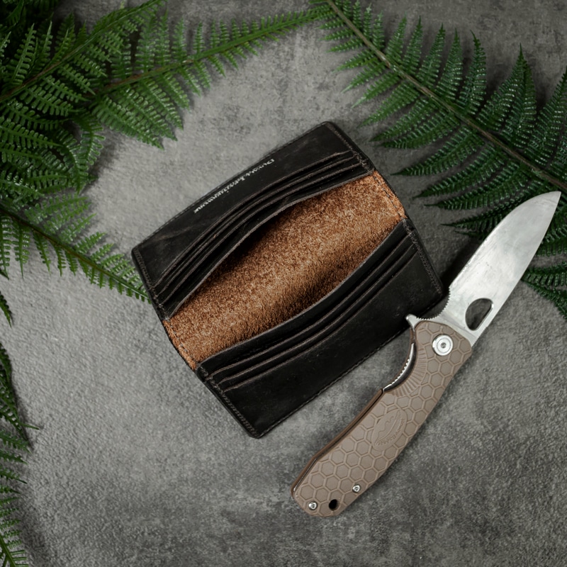 Inner pockets to a credit card wallet that can hold your cash or items for safe keeping shot with a pocket knife next to it and greenery on a slate tabletop.