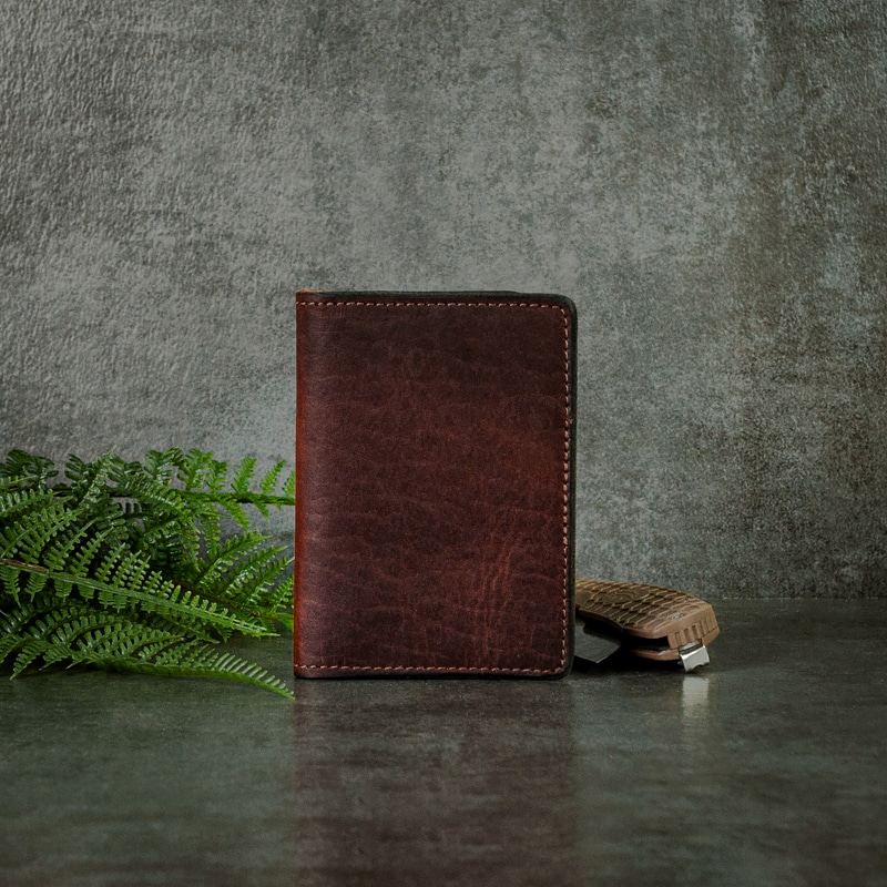 A credit card wallet that has an ID window for your identification or other cards made with dark mahogany leather shot on a slate background with fern and pocket knife.