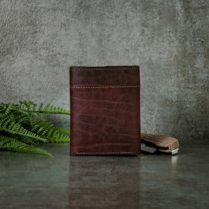 Back of a textured bison trifold wallet with a grey slate background shown with a pocket knife and greenery.