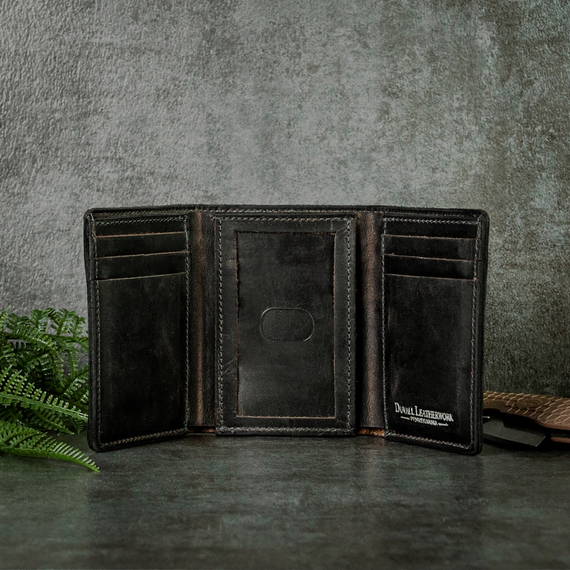 Inside of a sturdy trifold wallet that has multiple card slots and has an ID window in middle with fine stitching along the sides shot on a grey slate background with greenery and pocket.
