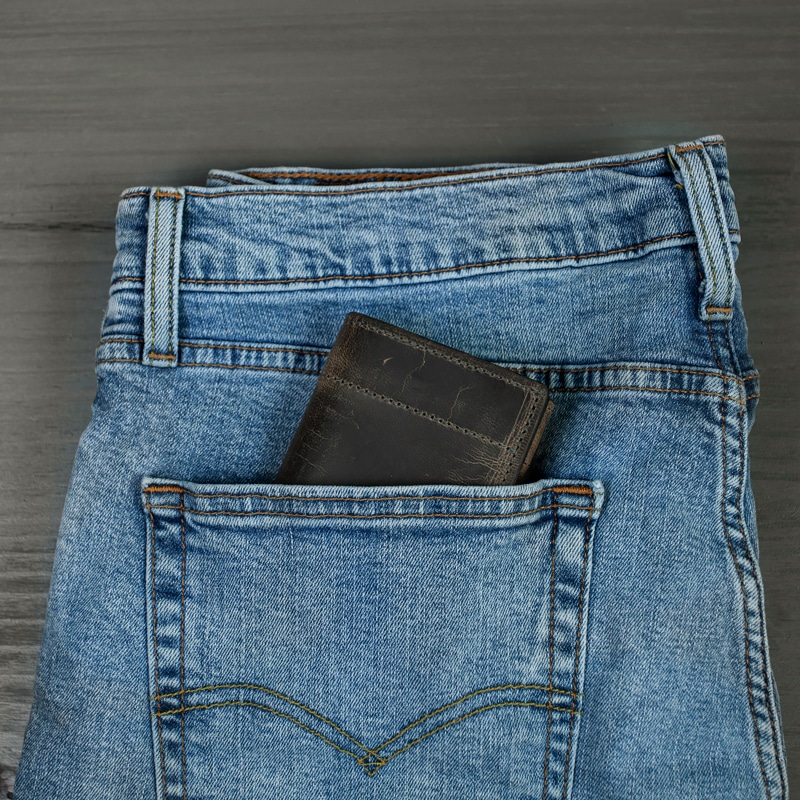 Trifold wallet in blue jeans back pocket perfectly for his every day use shot on a grey wood tabletop.