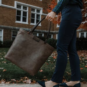 Woman walking with tote bag in front of a brick building during Fall.