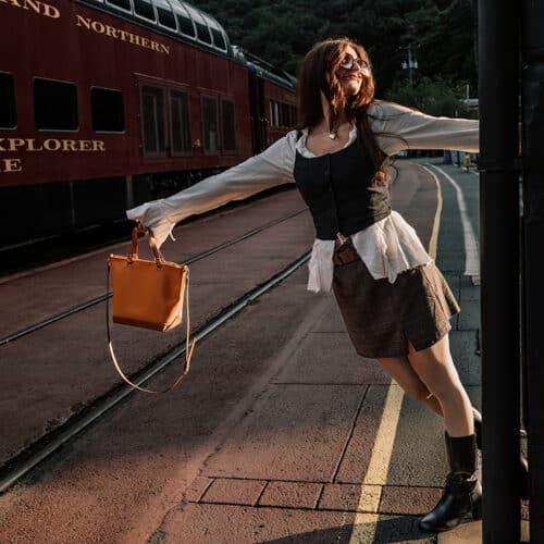 Woman holding orange and tan purse in front of a train