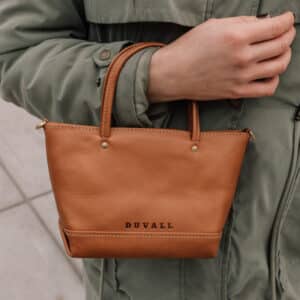 Woman holding a small tan leather mini handbag