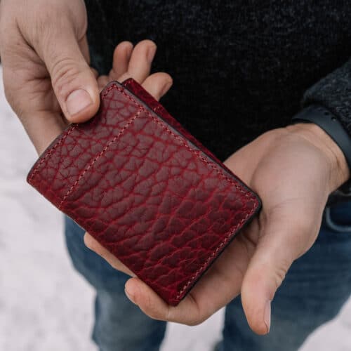 Red, Textured Bison Trifold Wallet being held in a man's hands to show the folded exterior cover of the wallet.