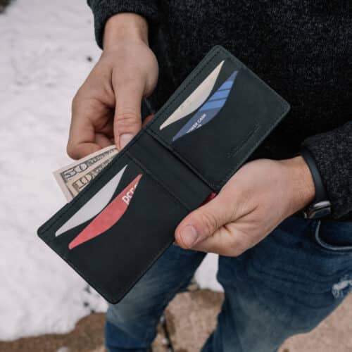 Red Bison Bifold Wallet opened in a man's hands to show the black goatskin leather interior filled with credit cards and cash.