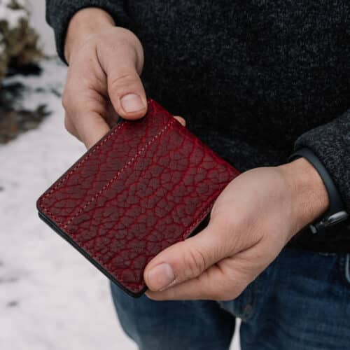 Red, Textured Bison Bifold Wallet being held in a man's hands to show the folded exterior cover of the wallet.