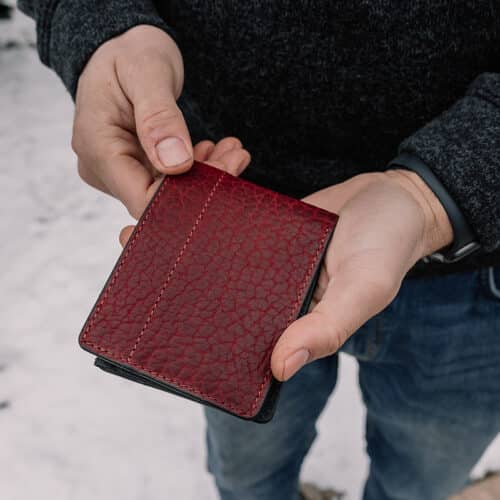 Red, Textured Bison Bifold Wallet with ID Window being held in a man's hands to show the folded exterior cover of the wallet.