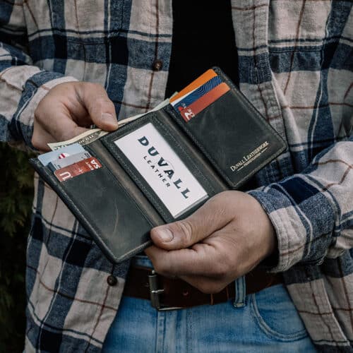 A close up of a man holding a green, leather trifold wallet to show the grey cowhide leather interior with the ID window.