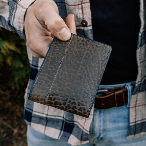 A man holding a green bison leather bifold wallet with ID window folded in his hands, showing off the exterior of the leather.