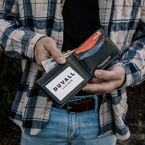 Man holding a green bison leather bifold with ID window wallet with a dark gray cowhide leather interior showing off the ID window, cash storage, and some of the card slots.