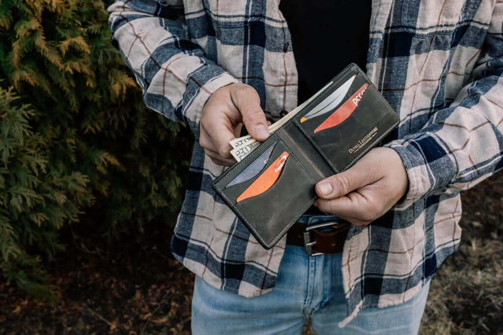 Man holding a green bison leather bifold with a dark gray cowhide leather interior showing off the card slots and cash storage.