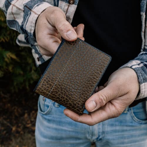 A man holding a green bison leather bifold wallet folded in his hands, showing off the exterior of the leather.