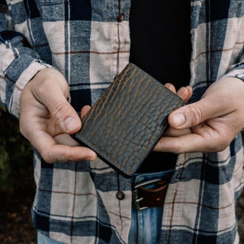 A man holding a small leather wallet showing of the green bison leather exterior.