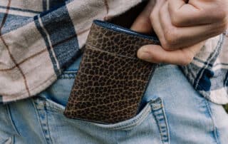 Close up photo of a man taking an olive green bison leather wallet out of his back pocket.