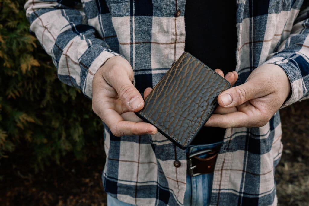 Man holding an olive green bison small wallet card case in his hands.